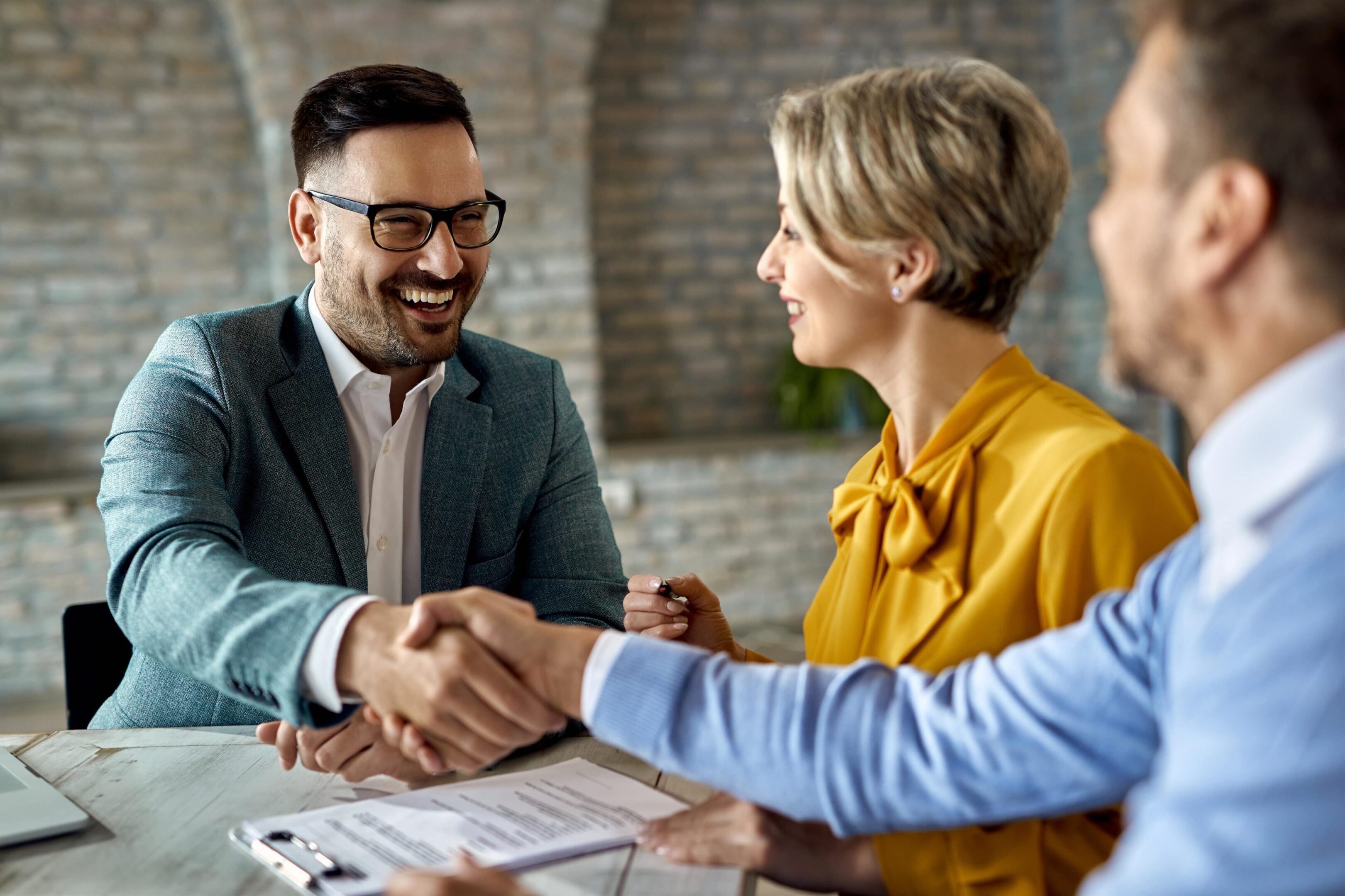 A man and woman shaking hands over papers.