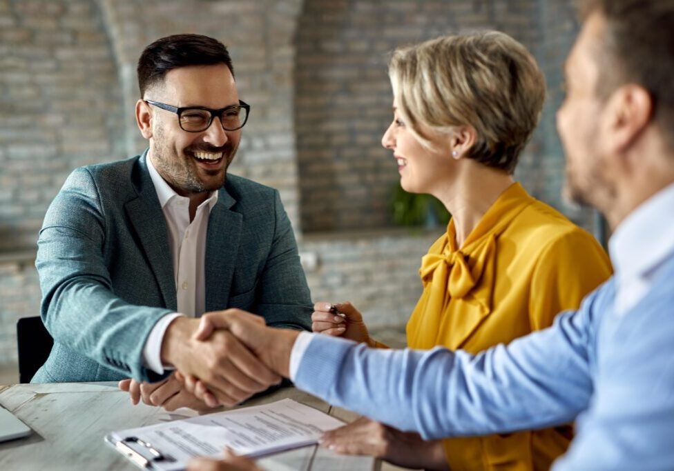 A man and woman shaking hands over papers.