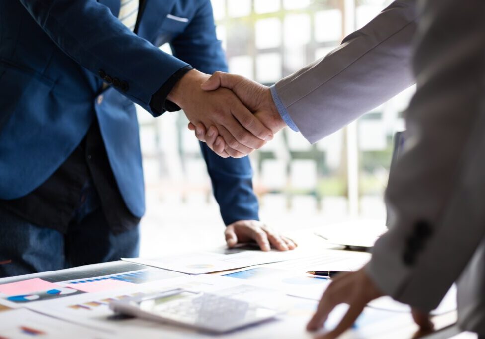 Two men shaking hands over a table with papers.